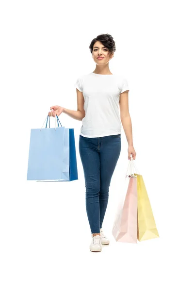 Mujer latina feliz de pie con bolsas de compras y sonriendo aislado en blanco - foto de stock