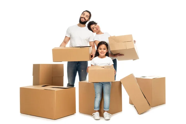 Alegres padres latinos sosteniendo cajas y de pie cerca de linda hija aislada en blanco - foto de stock