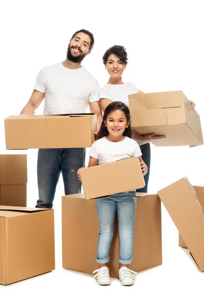 Cheerful latin parents holding boxes and standing with cute daughter isolated on white — Stock Photo