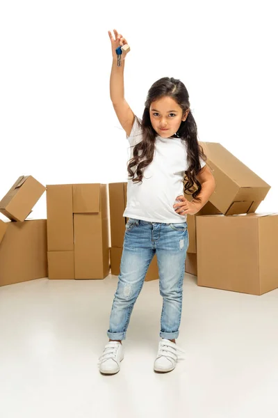 Niño latino feliz sosteniendo la llave y de pie con la mano en la cadera aislado en blanco - foto de stock