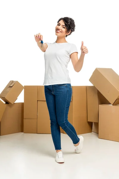 Low angle view of happy latin woman holding key and showing thumb up isolated on white — Stock Photo