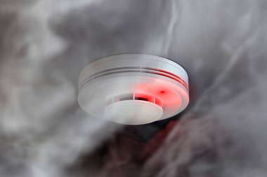 Dire alarm smoke detector with red LED indicator on ceiling clipart
