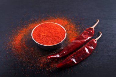 Red Chili pepper flakes and chili powder burst on black background