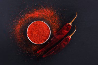 Red Chili pepper flakes and chili powder burst on black background