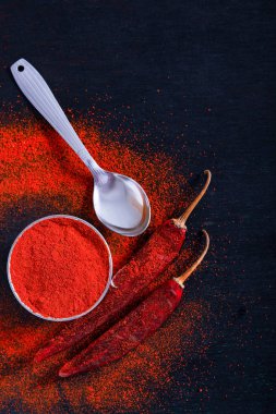 Red Chili pepper flakes and chili powder burst on black background