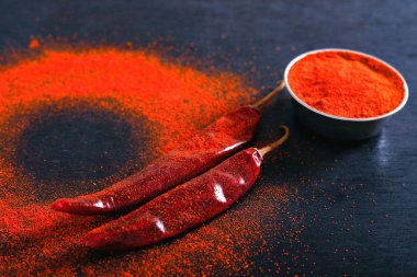 Red Chili pepper flakes and chili powder burst on black background