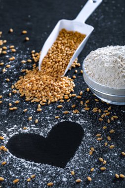 Composition with wheat grains, flour with heart shape on black background