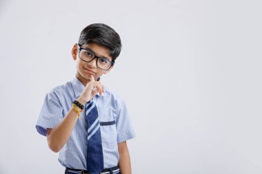 Cute little indian school boy asking / posing to keep silence, standing isolated over white background