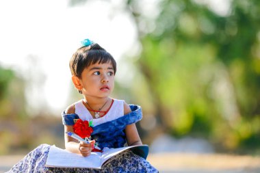 Indian Little Girl child writing on note book , studying 