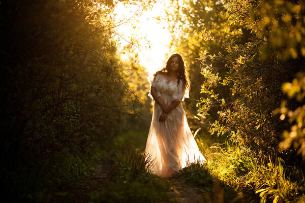 Beautiful young woman in a white dress at sunset