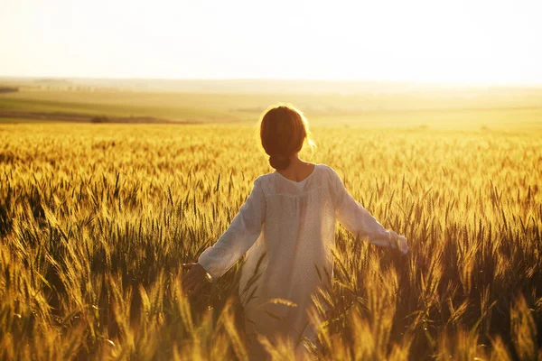 快乐的女人在傍晚的阳光下走过麦田 — 图库照片