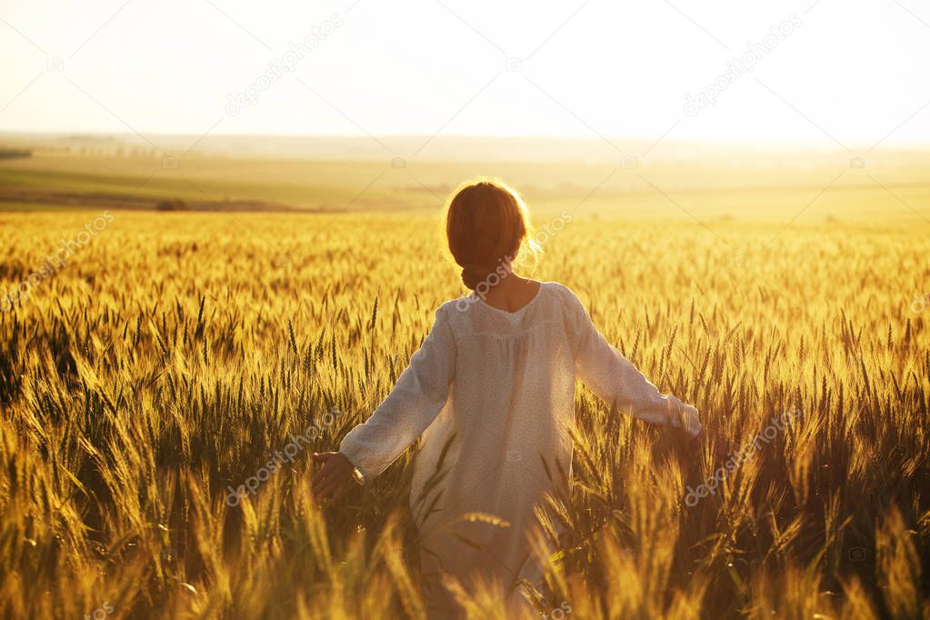 Happy woman walks over wheat field in the rays of the evening sun