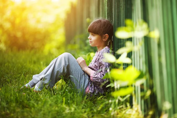 Mała dziewczynka siedzi na trawie w okresie letnim — Zdjęcie stockowe