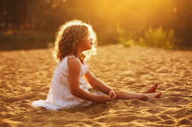 Oturma ve kumda oynayan küçük mutlu kız
