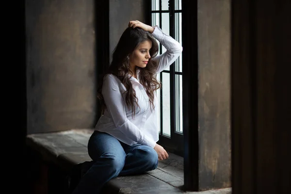 Femme en jeans s'assoit et regarde par la fenêtre — Photo