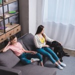 High angle view of woman with remote controller and her female friend embracing black labrador at home