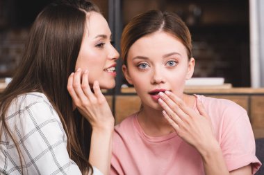 side view of young woman whispering secret to surprised female friend  clipart