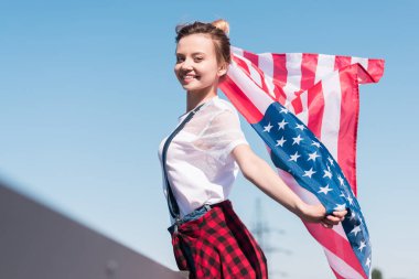 gülümseyen genç kadın Amerikan bayrağı mavi gökyüzü karşı bağımsızlık günü kavramı holding