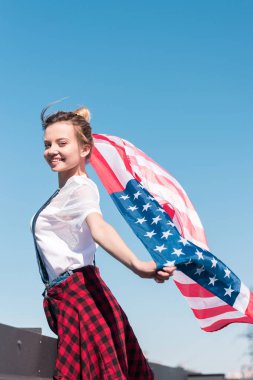 Amerikan bayrağı mavi gökyüzü karşı bağımsızlık günü kavramı tutan genç kadın