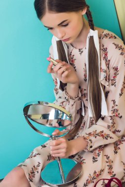 beautiful teen girl applying lipstick with mirror  clipart