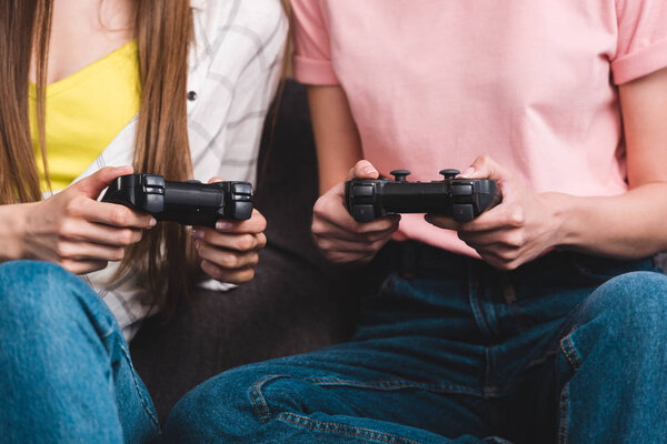 cropped image of two female friends  with joysticks in hands playing video game 
