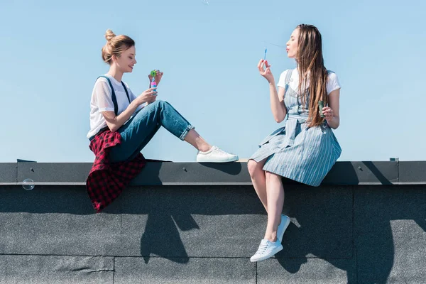 side view of two female friends using bubble blowers at rooftop