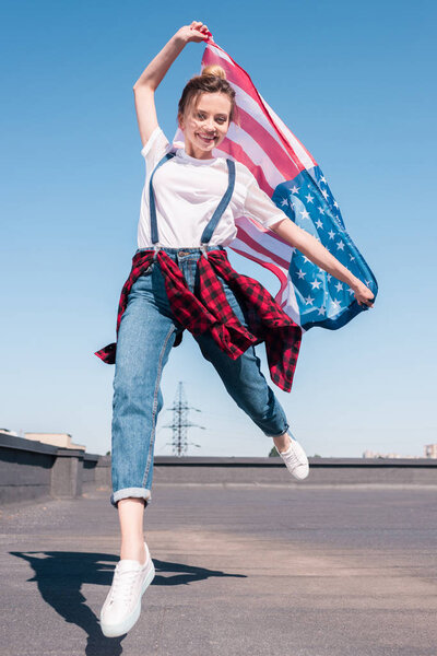 happy young woman jumping with United States flag at rooftop, independence day concept
 
