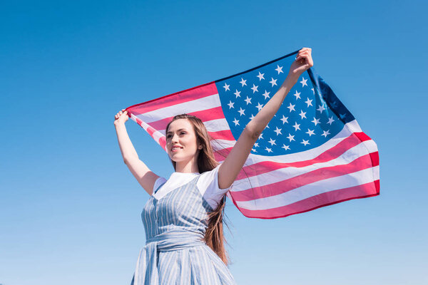 young woman holding american flag against blue sky, independence day concept
