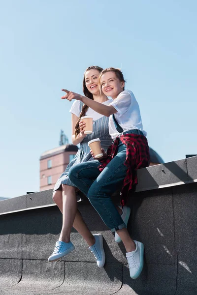 Mujer Joven Señalando Con Dedo Una Amiga Sonriente Con Una — Foto de stock gratuita