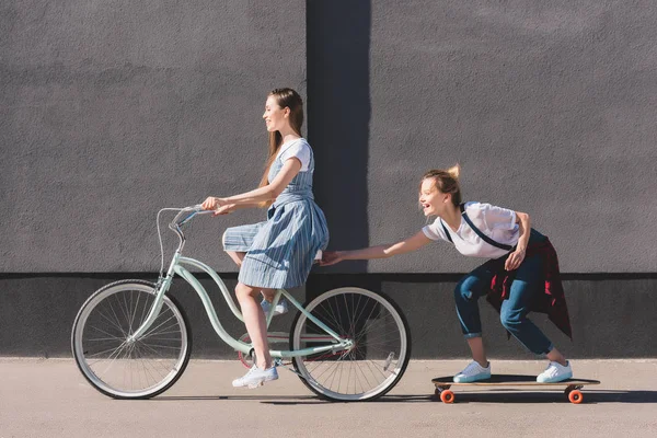 Vista Lateral Mujer Montando Bicicleta Remolcando Amiga Sonriente Monopatín — Foto de Stock