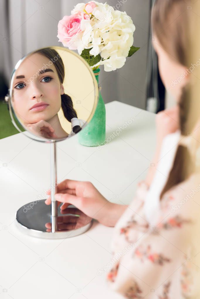 selective focus of teen girl with braids sitting at table and looking at mirror 