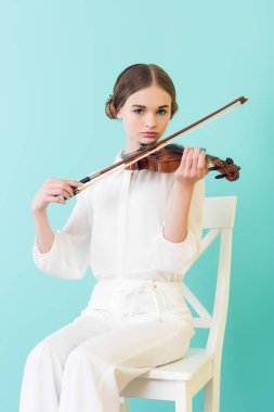 teen girl playing violin and sitting on chair, isolated on turquoise  clipart