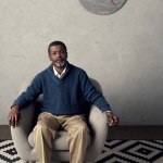 Guapo afroamericano hombre sentado en sillón en la habitación con reloj