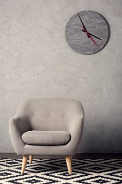 Koltuk, halı ve basit gri odasında duvar saati