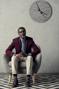 duvar saati ile koltukta oturan düşünceli Afrikalı-Amerikalı adam  