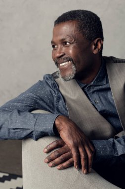 yakışıklı gülümseyen orta yaşlı Afrikalı-Amerikalı adam koltuğa oturan yelek portresi