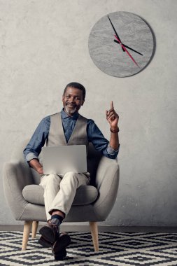 yukarı dönük ve dizüstü bilgisayar kullanma office duvar saati ile şık Afrikalı-Amerikalı iş adamı