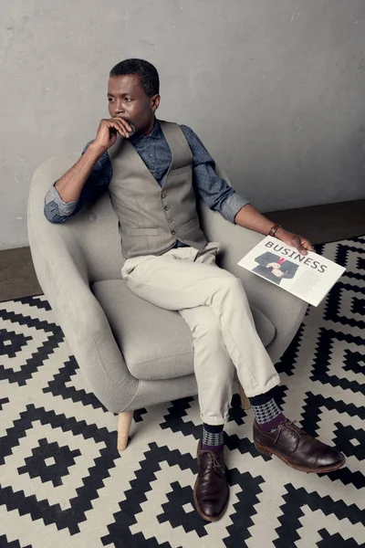 ビジネス新聞の肘掛け椅子に座っているチョッキでスタイリッシュなアフリカ系アメリカ人 — ストック写真