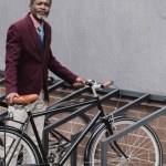 Homem de negócios americano africano maduro na moda com bicicleta no estacionamento para bicicletas