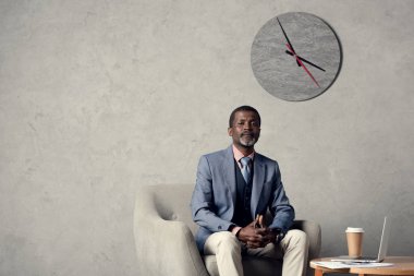 kendine güvenen orta yaşlı Afrikalı-Amerikalı işadamı gazete, kahve ve dizüstü bilgisayar ile mavi ceketli 