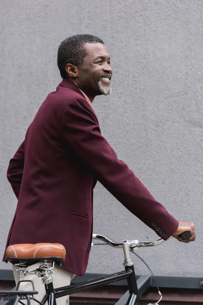 Стильный Улыбающийся Африканский Американец Бордовом Пиджаке Позирует Возле Велосипеда — Бесплатное стоковое фото