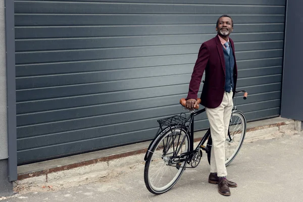 时髦的非洲裔美国人男子在勃艮第夹克摆在自行车附近 — 图库照片