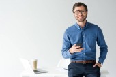 pohledný mladý podnikatel s smartphone se zpět na pracovišti izolované na bílém