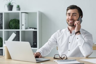İşyerinde telefonla konuşurken ve kameraya bakarak genç işadamı gülümseyen