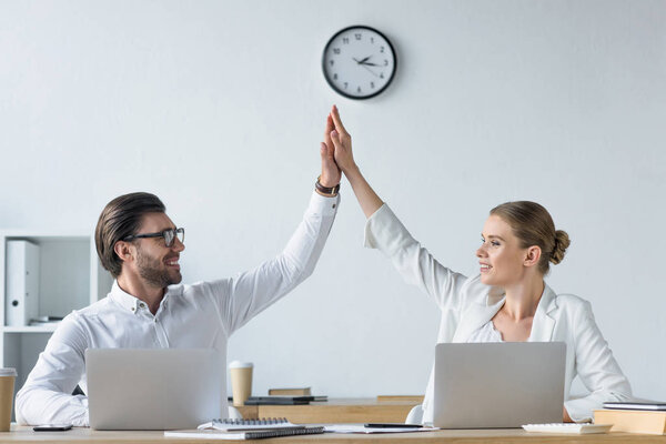 счастливые успешные менеджеры, работающие вместе с ноутбуками в офисе и дающие пять
