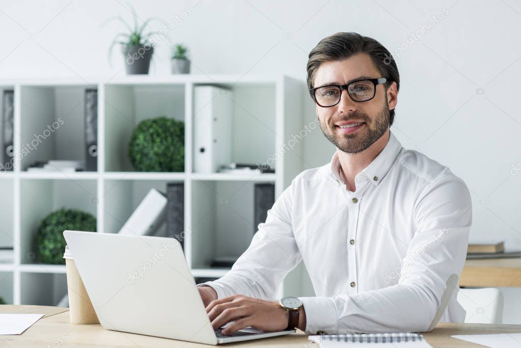 happy young businessman working with laptop at modern office and looking at camera