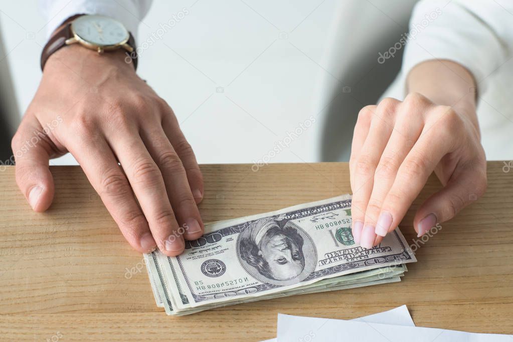 cropped shot of business partners holding stack of cash on table