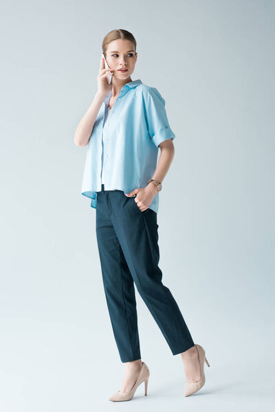 attractive young woman in blue shirt talking by phone on grey