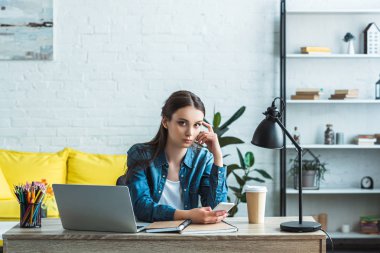Smartphone kullanarak ve dizüstü bilgisayar ile evde okurken kameraya bakarak çekici kız