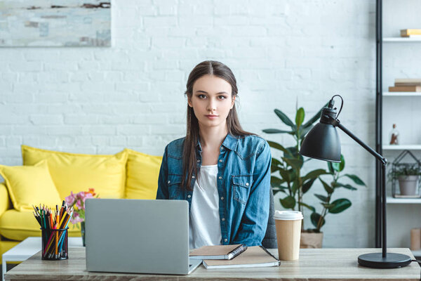 beautiful girl using laptop and looking at camera while studying at home